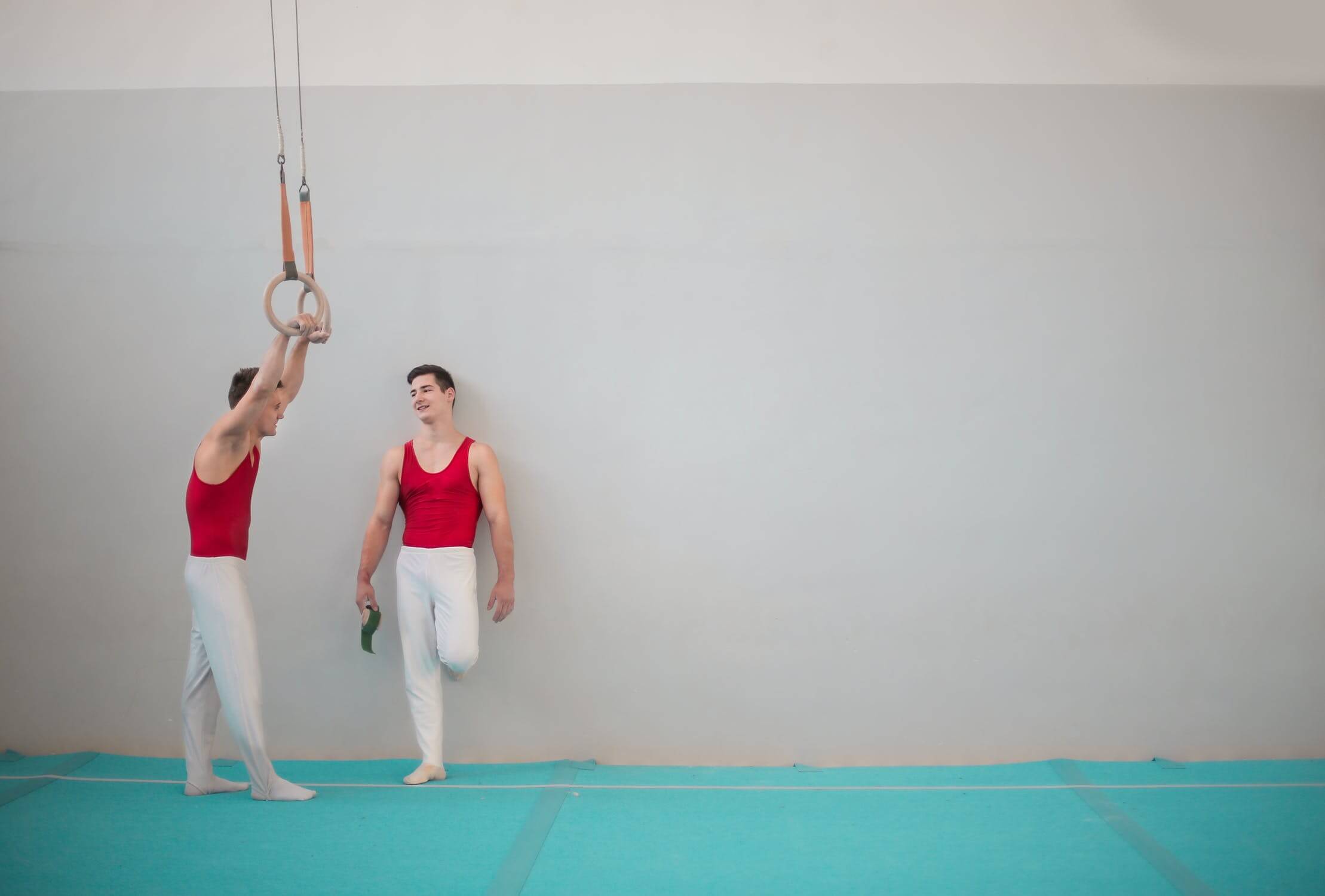 gymnasts standing talking, one holding gym rings